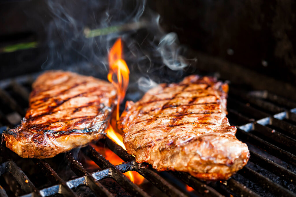 two steaks cooking on a portable gas grill